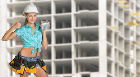 Young woman in hard hat holding calculator and looking at camera. Industrial backgroundの写真素材