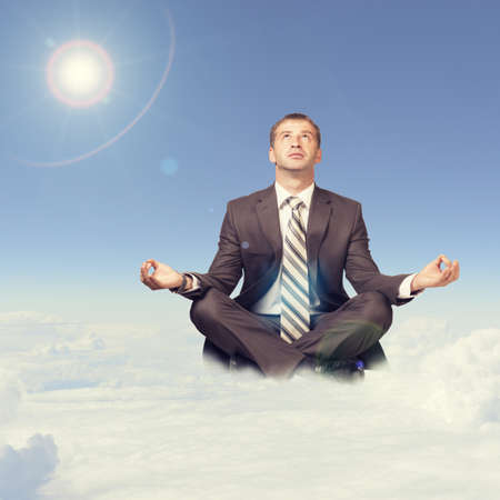 Businessman sitting in lotus position on cloud and looking upの写真素材