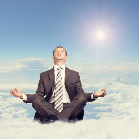 Businessman sitting in lotus position on cloud and looking upの写真素材