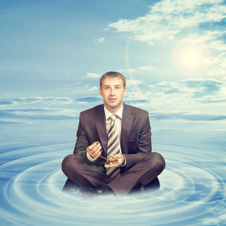 Businessman sitting in lotus position on cloud with oil lamp and looking at cameraの写真素材