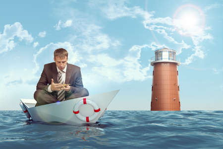 Businessman sitting in lotus position in paper boat in sea and looking at oil lampの写真素材