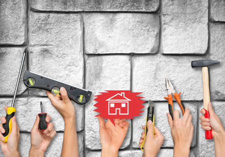 Set of peoples hands holding different tools and computer icons on old grey brick wall texture...
