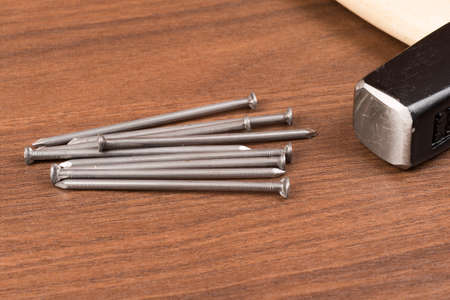 Hammer and nails on brown wood table, close-up view