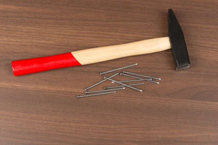 Hammer with red handle and nails on brown wood table, close-up view