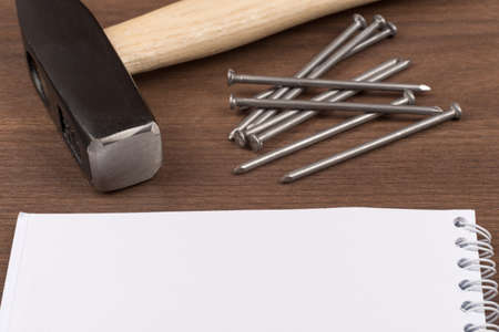 Hammer with set of scattering nails and note pad on brown wood table, close-up viewの写真素材