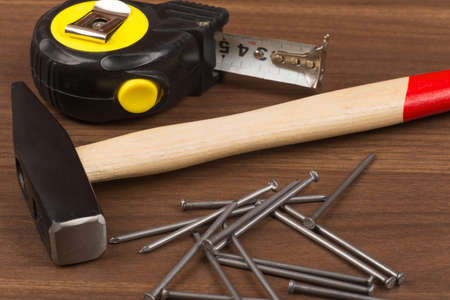 Hammer with steel tape and nails on brown wood table, close-up viewの写真素材
