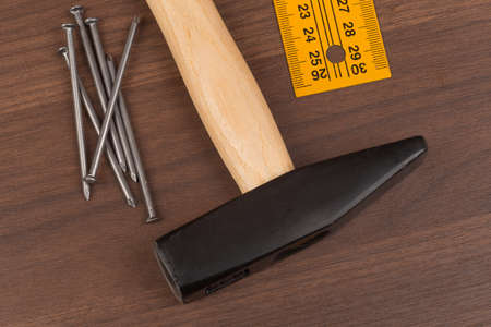 Hammer with ruler and nails on brown wood table, close-up view