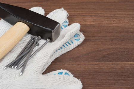 Hammer with protective gloves and nails on brown wood table, close-up viewの写真素材