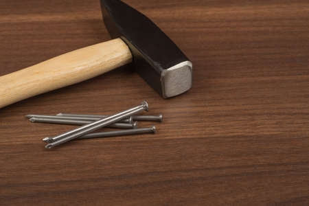 Hammer with pile of nails on brown wood table, front view