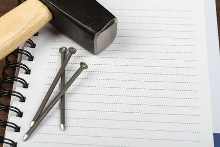 Hammer with three nails and note pad on brown wood table, top viewの写真素材