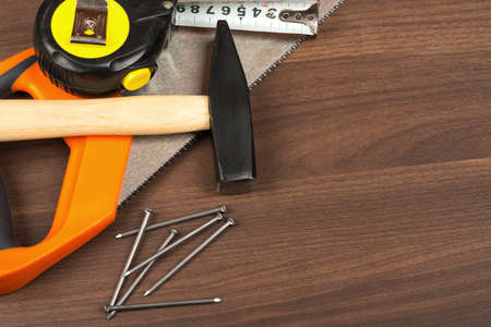 Hammer with steel tape and saw on brown wood table, side view