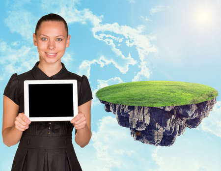 Businesswoman with tablet and island in sky with clouds and green grassの写真素材