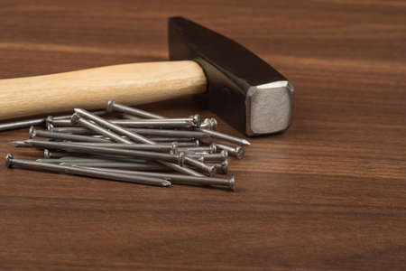 Hammer with big pile of nails on brown wood table, front view