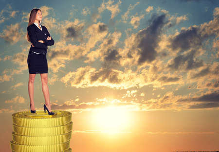 Businesswoman standing on coins stack and looking upの写真素材