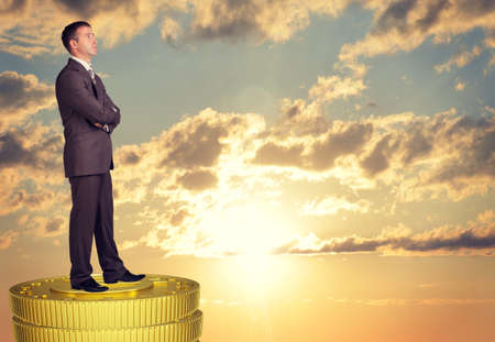 Thoughtful businessman standing on coins stack and looking upの写真素材