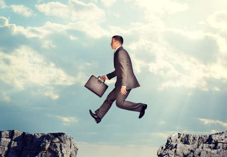 Businessman with suitcase jumping over precipice on nature backgroundの写真素材