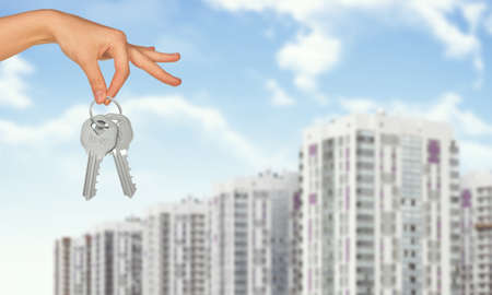 Hand holding keys on cityscape background under blue sky with cloudsの写真素材
