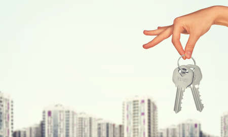 Hand holding keys and cityscape on white backgroundの写真素材
