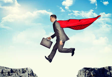 Businessman with suitcase and cloak hopping abyssの写真素材