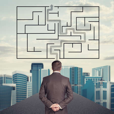 Businessman with crossed hands, labyrinth and cityscape background, back viewの写真素材