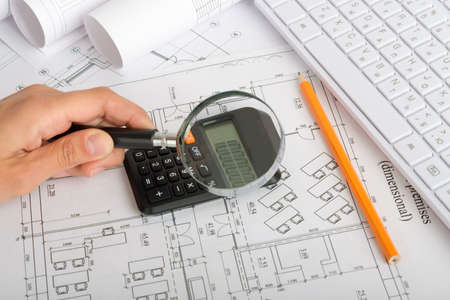 Human looking at draft using magnifier. Calculator and pencil on tableの写真素材