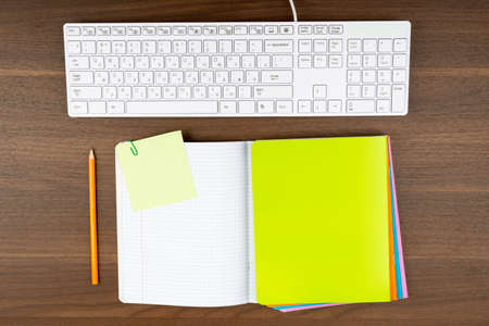 Keyboard with notebooks and pencil on wooden tableの写真素材