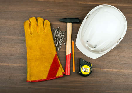Construction gloves with hammer and helmet on wooden table