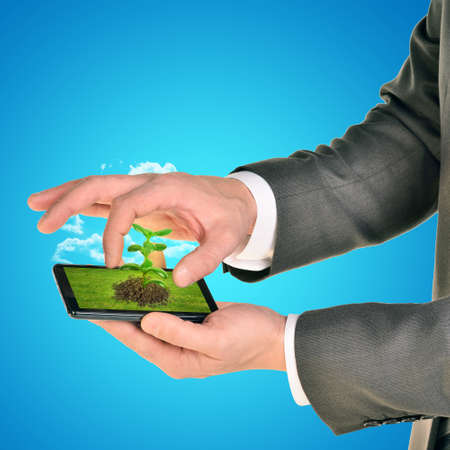 Businessman holding smartphone with plant on blue backgroundの写真素材