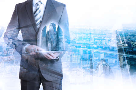 Business person holding tablet with 3d city model on cityscape backgroundの写真素材