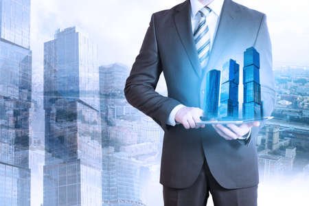 Businessman holding tablet with 3d city model on cityscape backgroundの写真素材