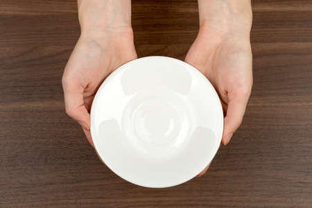 Womans hands holding saucer on wooden table backgroundの写真素材