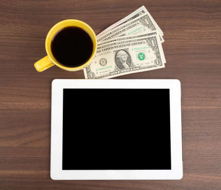 Tablet with coffee and money on wooden tableの写真素材