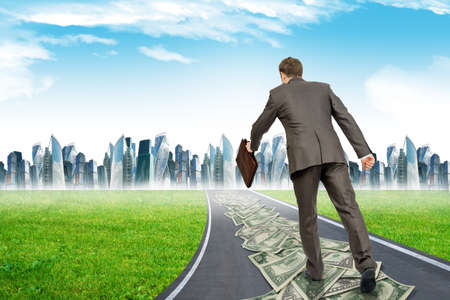 Businessman on money road running to city, rear viewの写真素材