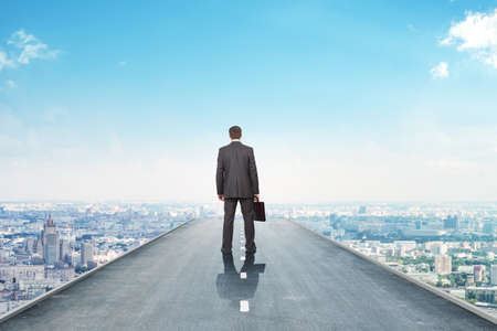 Businessman on road with city, rear viewの写真素材
