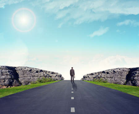 Businessman on road with mountains, rear viewの写真素材