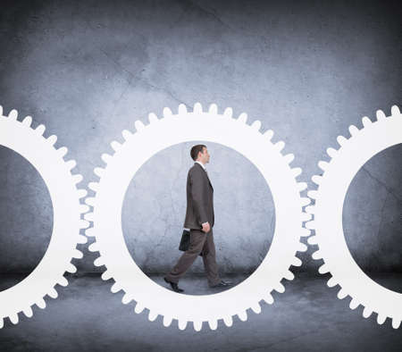 Businessman walking in cog wheel on abstract backgroundの写真素材