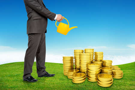 Businessman with can watering coins with green grass and blue skyの写真素材