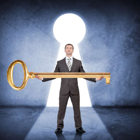 Businessman in suit holding huge gold keyの写真素材