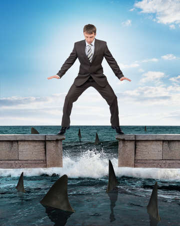 Businessman in suit standing above sharks in waterの写真素材
