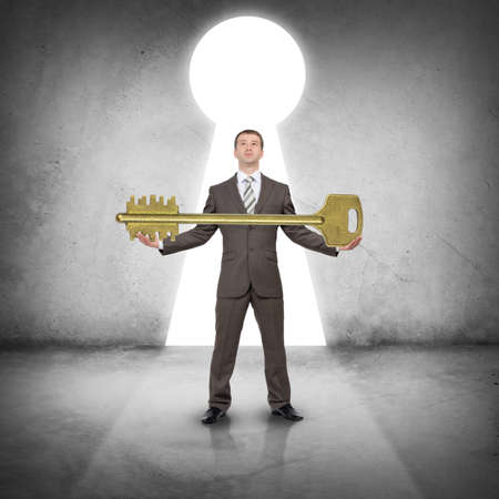 Businessman in suit holding huge gold keyの写真素材