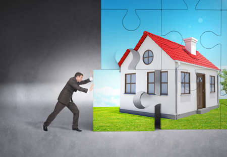 Man pushing puzzle piece of house picture on grey background
