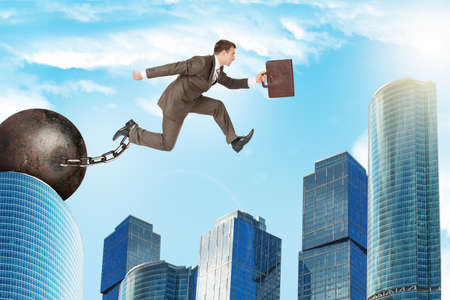 Businessman with iron ballast hopping over city