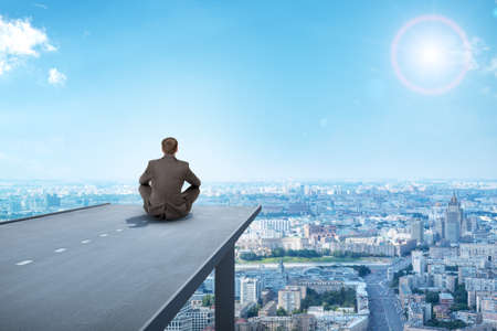 Businessman sitting on road with city, rear viewの写真素材