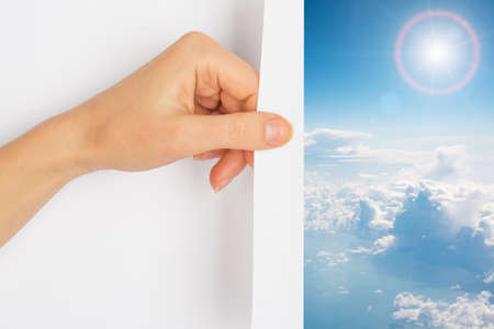 Hand turning the page revealing blue skies and clouds