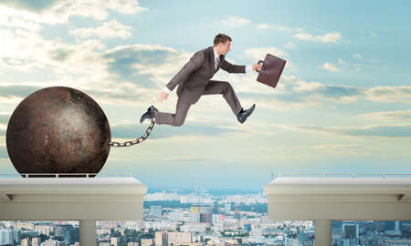 Image of young businessman with suitcase and iron ballast jumping over gapの写真素材
