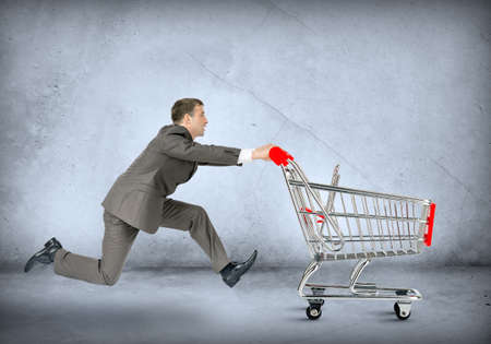 Businessman pushing shopping cart on grey wall backgroundの写真素材