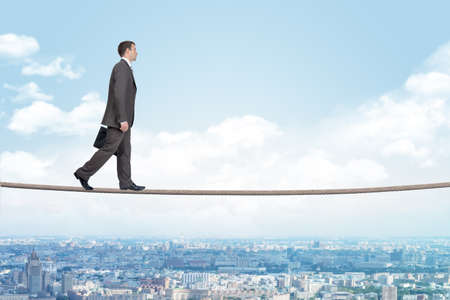 Businessman walking on rope above city with closed eyesの写真素材