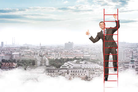 Smiling businessman climbing ladder on blue sky backgroundの写真素材