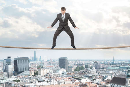 Businessman standing on rope above city looking downの写真素材