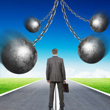 Businessman with set of iron balls standing on roar, rear viewの写真素材